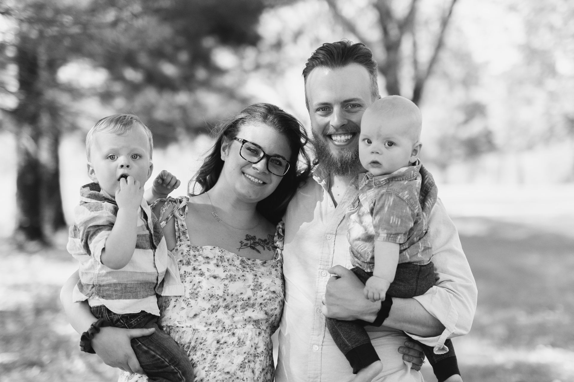 Black and white photo of a smiling family standing outdoors, with two adults holding two young children.